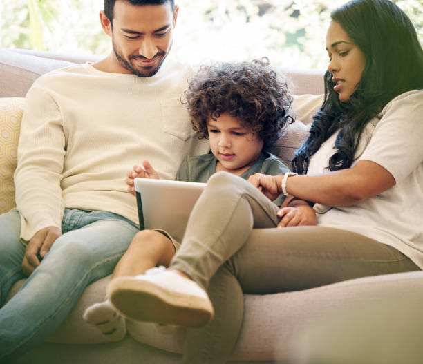 istock Shot of a little boy using a digital tablet while sitting at home with his parents 1395821643