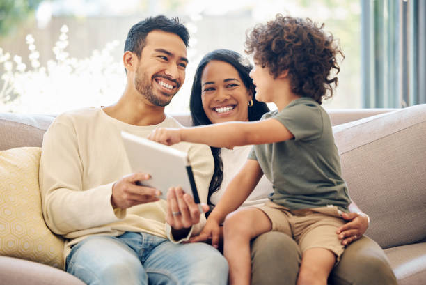 photo d’un petit garçon utilisant une tablette numérique alors qu’il était assis à la maison avec ses parents - holding men casual mother photos et images de collection