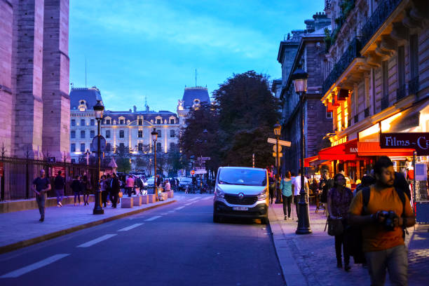 wieczór na ile de la cite, gdy paryżanie i turyści robią zakupy wśród oświetlonych sklepów i kawiarni z katedrą notre dame po drugiej stronie ulicy. - paris france notre dame night ile de la cite zdjęcia i obrazy z banku zdjęć