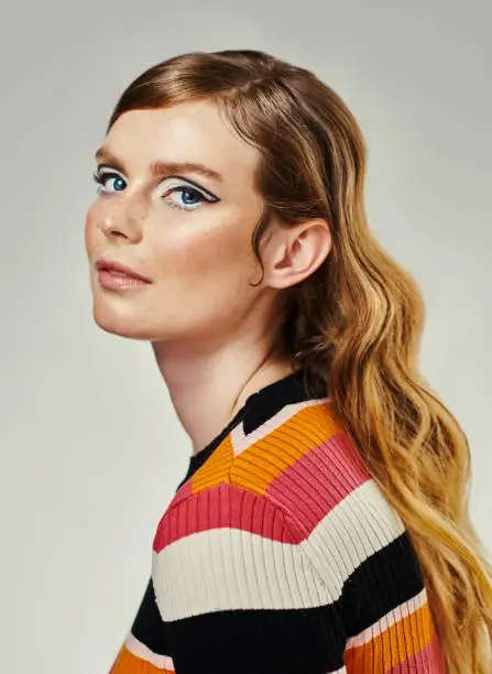 Photo of An attractive young woman dressed up in 60’s wear against a grey studio background. Portrait of a beautiful model looking at the camera dressed in a retro style