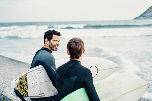 Father and son holding surf board at the beach. Happy family going surfing together