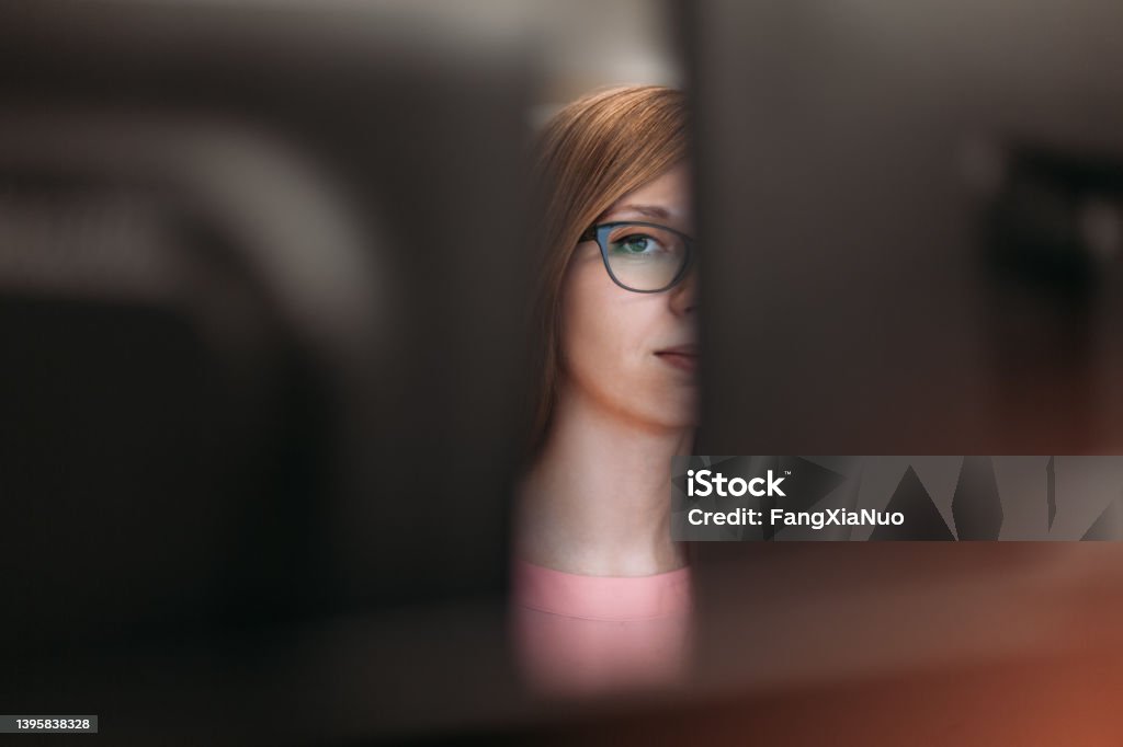 Woman peeking through computer monitors in office Privacy Stock Photo