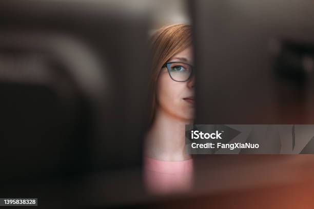 Woman Peeking Through Computer Monitors In Office Stock Photo - Download Image Now - Privacy, Envy, Hiding