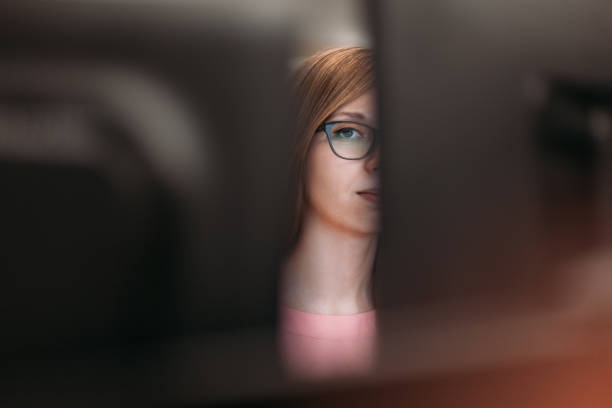 woman peeking through computer monitors in office - inveja imagens e fotografias de stock