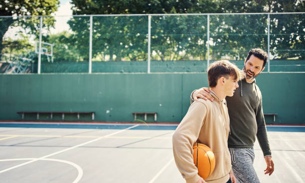 아버지와 아들은 농구 게임을 한 후 걷고 있습니다. 젊은 남자와 십대 소년은 재미 있고, 말하고, 채팅하면서 건강하고, 활동적입니다. - child discussion parent talking 뉴스 사진 이미지
