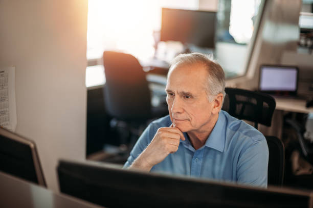 istock Senior businessman contemplating data on computer screen while smiling to make decisions in office 1395838344