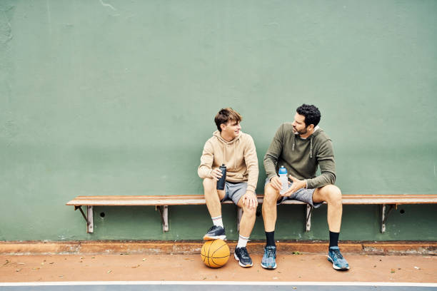 father and son taking a break after playing a game of basketball. young man and teenage boy talking and drinking water - teenager parent father son imagens e fotografias de stock