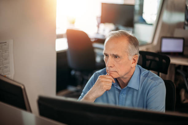Senior businessman contemplating data on computer screen to make decisions in office stock photo