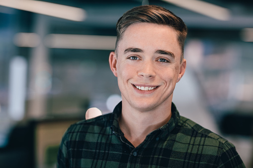 Young handsome male businessman looking away and holding digital tablet inside modern office