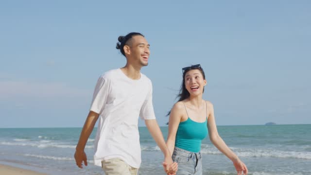 Asian young man and woman having fun, playing on the beach together. Attractive new marriage people feel happy while walking and running at seaside enjoy holiday honeymoon trip in tropical sea island.