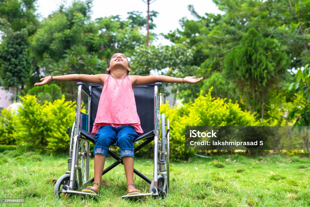 concept of freedom, individuality and courage showing by Happy girl kid feeling nature by stretching arms while using wheelchair at hospital park. Child Stock Photo