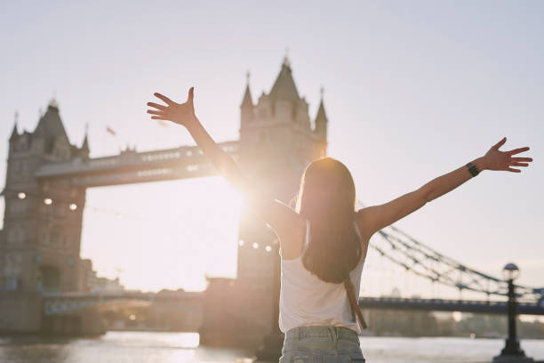 ロンドンのタワーブリッジの隣に立ち、日没時に歓声を上げる女性のバックビューショット - tower bridge uk london england people ストックフォトと画像