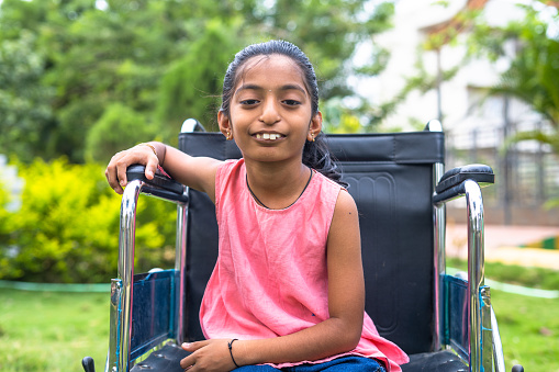 Concept of recovery and optimism showing with happy smiling kid with disability on wheelchair confidently looking camera at park