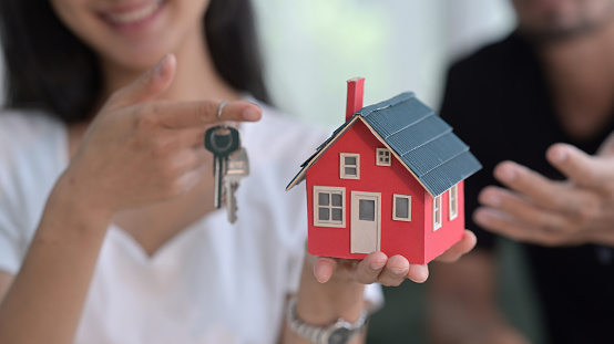 Front view of happy young couple holding house model and keys. New house, insurance and real estate concept.