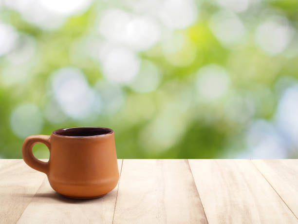 côté de tasse à café en argile brune vintage cuite sur table en bois avec bokeh de lumière naturelle de la lumière du soleil entre feuilles vertes - brown table coffee table side table photos et images de collection