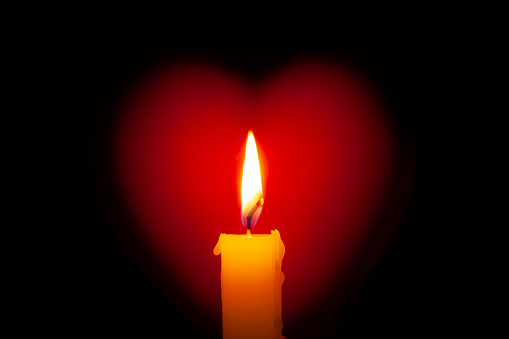 Candle with heart on black background.