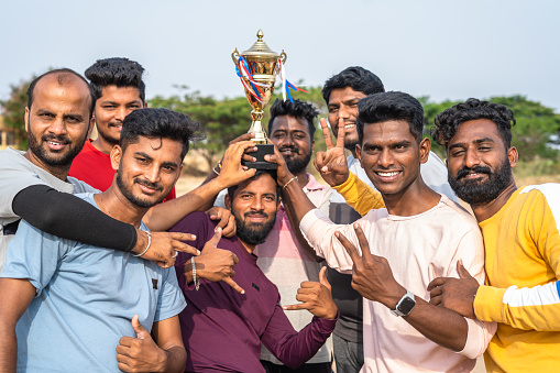group of cricket players celebrating victory of cricket match by holding trophy and by lifting captain - concept of excitement, championship and competition