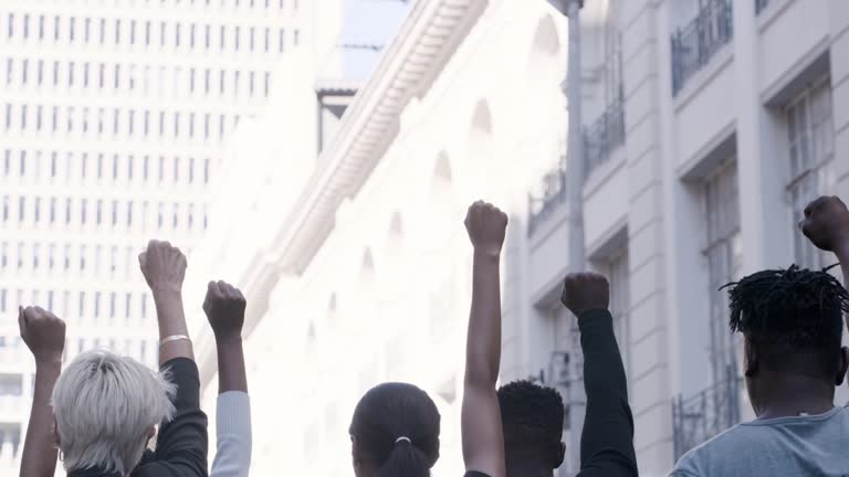 Diverse group of people walking together down the street during a protest. Crowd of people raising their fists in solidarity as they march together at a rally