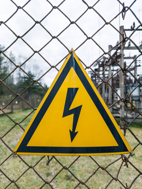 istock Yellow electricity warning sign with lightning hanging on rustic wire mesh fence. 1395854388