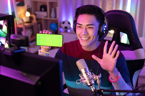 asian man internet celebrity have a live stream and show app on the smartphone with green screen at home