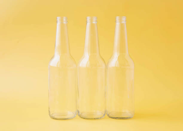 Three empty glass beer bottles stand on a bright yellow background.