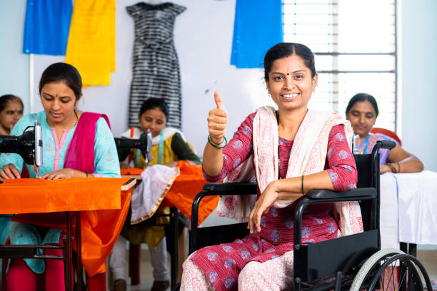 happy smiling woman with disability showing thumbs up gesture at garments using wheelchair - concept of small business owner, inspiration and employment. - factory garment sewing textile imagens e fotografias de stock