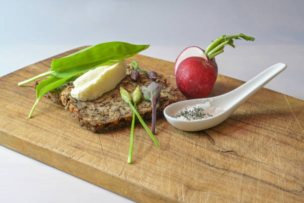 Whole grain bread with butter, radish, herb salt and wild garlic on a rustic wooden cutting board, simple healthy and natural meal, copy space, selected focus stock photo