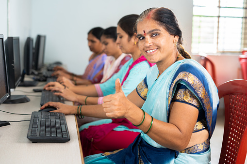 Smiling women showing thumbs up by looking camera during computer training class - concept of women employment, learning and education.