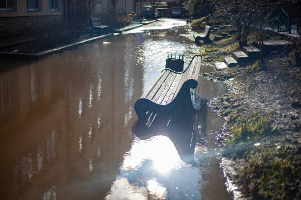 Bench stands in puddle. Spring flood. Shop in park. Place to relax in city.