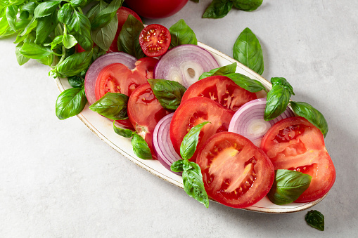 Salad with tomatoes, basil, and red onion on a kitchen table.