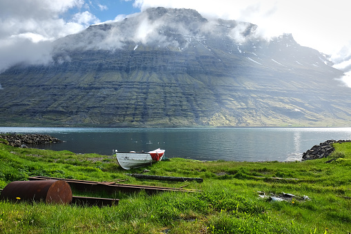 Rowboat moored on the grassy shore in Eskifjörður fjord, Iceland. cloud-covered Hólmatindur mountain in the background