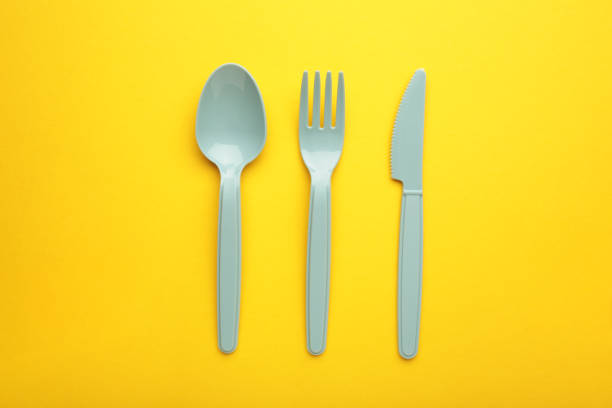 istock Blue plasic forks, spoons and knives on yellow background with copy space, top view. 1395868792