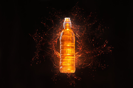 Energy drink isotonic for athletes and people who play sports. It helps to keep the body in tone during training. Isotonic energy drink. Orange bottle on black background with splashes