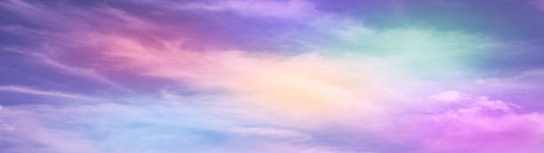 Rainbow sky with fluffy clouds. Abstract purple green yellow background with space for design. Multicolored toned sky.