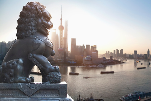 Chinese Temple Foo Dog Lion guard statue with Shanghai's Pudong District's skyscrapers in the morning with barges, Oriental Pearl Tower, Shanghai World Financial Center, Shanghai Tower, and Jin Mao Tower, retouched digital composite image