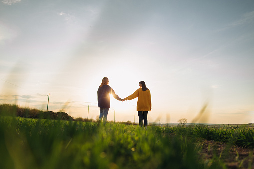 Two women wearing a Ukrainian national color sweatshirts walking on the field at the sunset