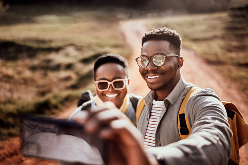 Smiling young male hiker wearing eyeglasses taking selfie with girlfriend over smart phone