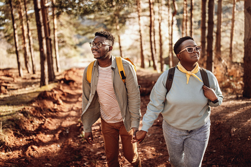 Young couple wearing glasses holding hands while hiking against trees in woodland