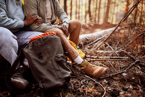 Young couple with backpacks and insulated drink container sitting on log against trees in forest
