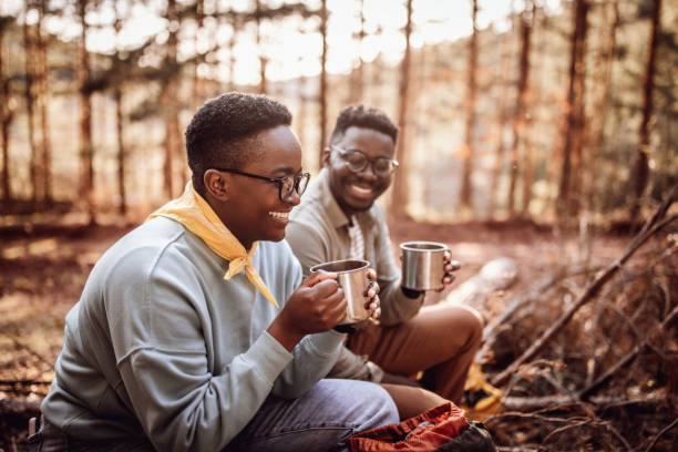 istock Smiling couple with mugs sitting against trees in forest 1395877272