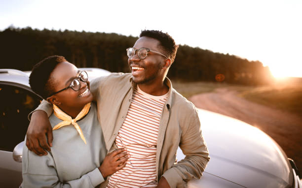 Man with hand on girlfriend's shoulder standing by car at sunset stock photo