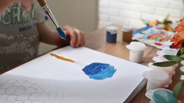 child drawing lollypop with blue gouache paint in album