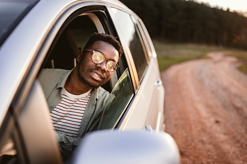 Young man wearing eyeglasses peeking through window while sitting in car during sunset