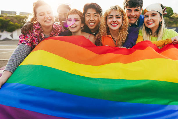 Young diverse people having fun holding LGBT rainbow flag outdoor - Focus on center blond girl stock photo