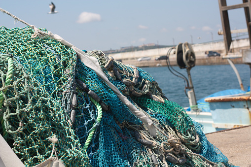 Pile of fishing nets with floats on a quay with blurred boats on background. Şile, İstanbul