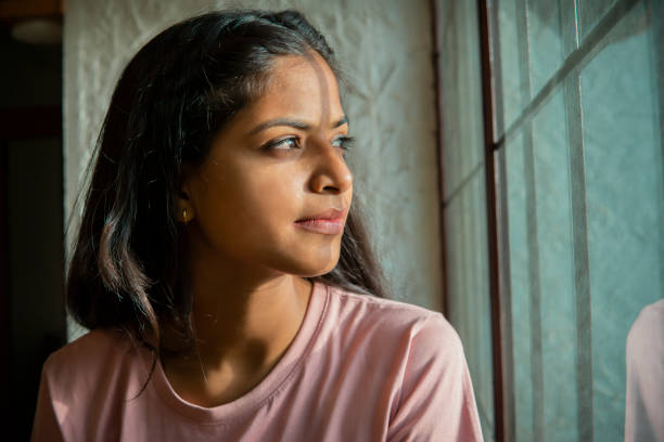 Indoor close-up portrait of beauty, Asian, Indian serene young woman sitting near the window and contemplating while looking out through the window. Indoor close-up portrait of beauty, Asian, Indian serene young woman sitting near the window and contemplating while looking out through the window. soul searching stock pictures, royalty-free photos & images