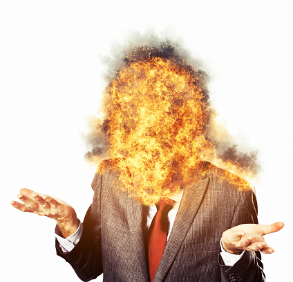 Businessman wearing a smart suit and tie makes a resigned gesture as his head burns, perhaps a result of emotional stress or overwork.