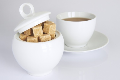 white sugarbowl with brown sugarcubes and a cup of tea