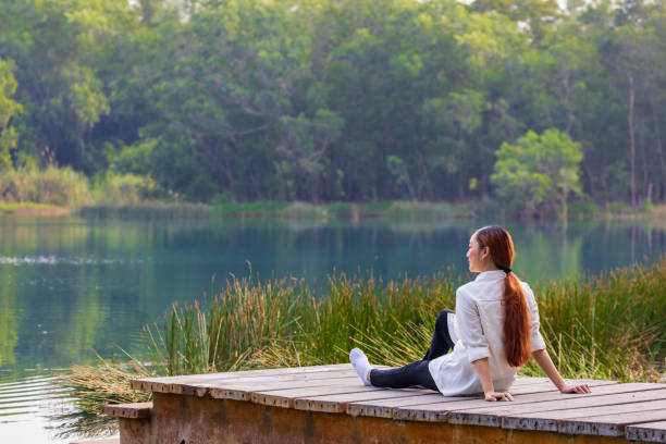 asiatische frau sitzt im sommer am rande des docks mit friedlichem naturpark und blickt auf den türkisfarbenen see für ruhige und entspannende erholung im freien - lake tranquil scene landscape zen like stock-fotos und bilder