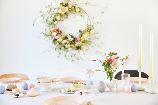 A modern table decoration as an Easter table with a floral Easter wreath hanging on the wall in a bright, large room. Photographed in high resolution